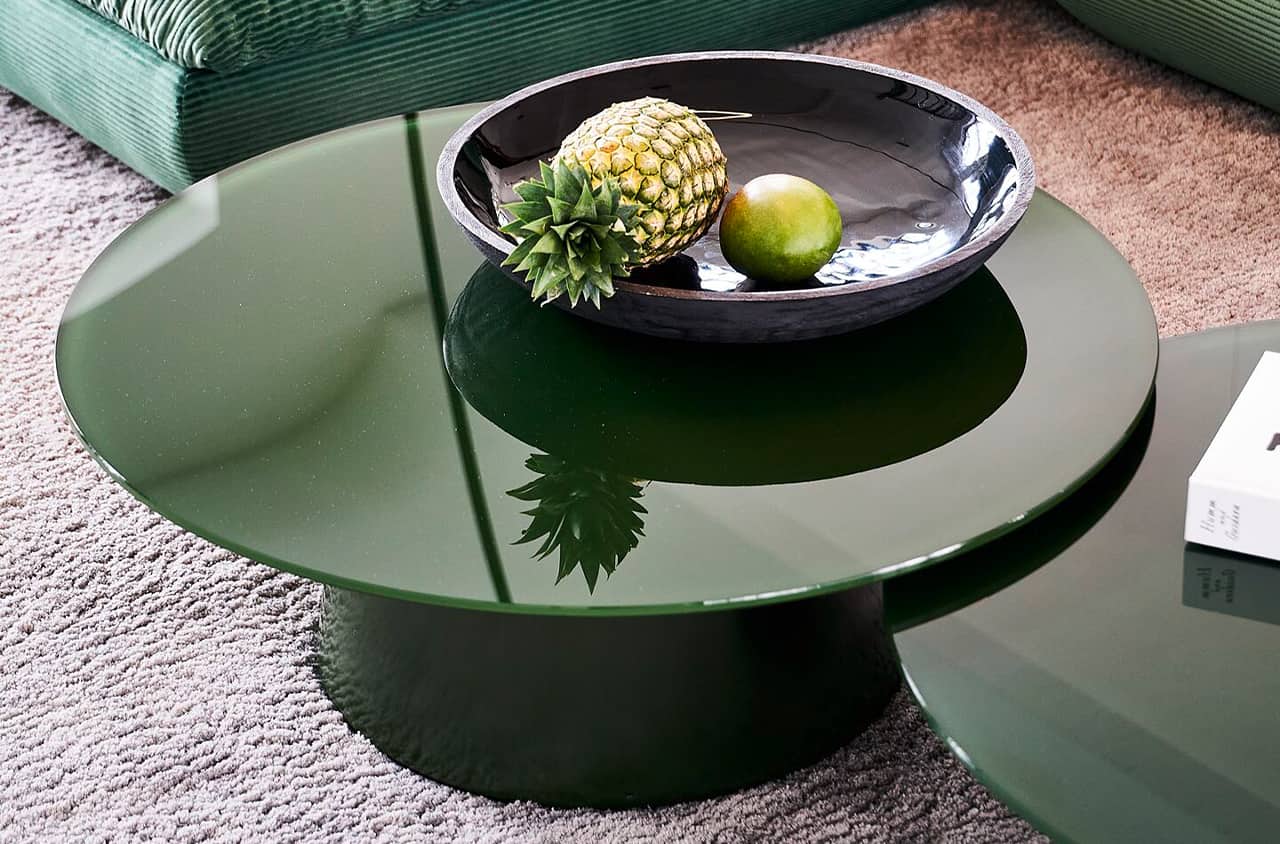 Grüner runder Couchtisch mit glänzender Oberfläche und zylindrischem Fuß in moderner Wohnumgebung mit Teppich.